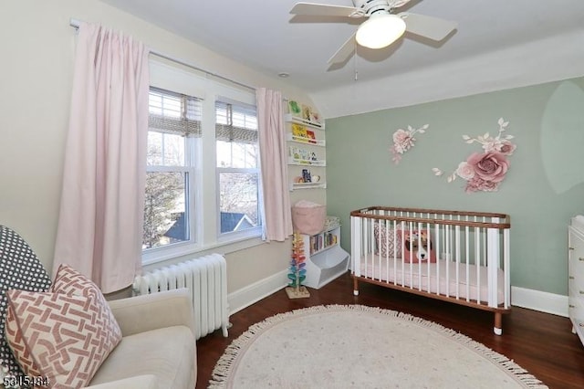 bedroom with a crib, baseboards, radiator, lofted ceiling, and dark wood-type flooring