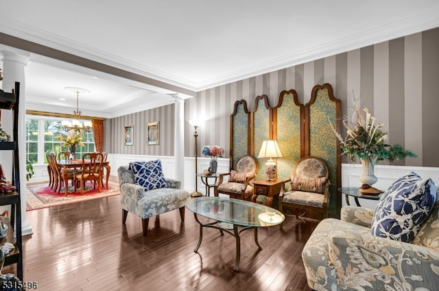 living room featuring hardwood / wood-style floors, crown molding, an inviting chandelier, and decorative columns