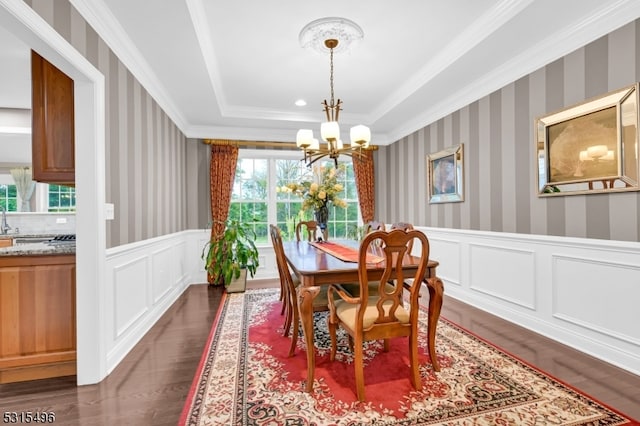 dining space featuring sink, a tray ceiling, dark hardwood / wood-style flooring, crown molding, and a chandelier