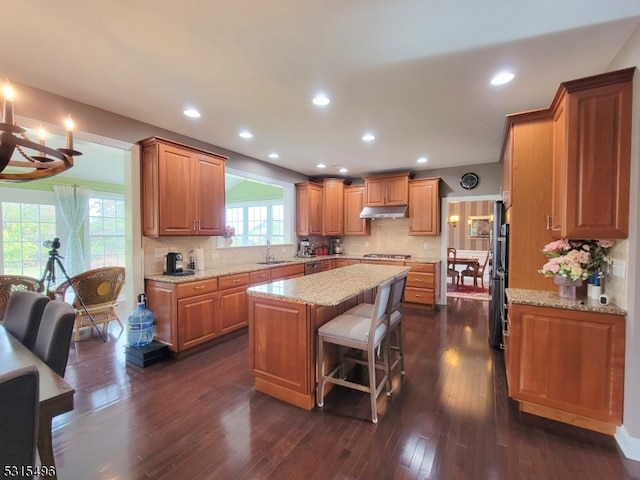 kitchen with light stone counters, a kitchen island, dark wood-type flooring, and tasteful backsplash