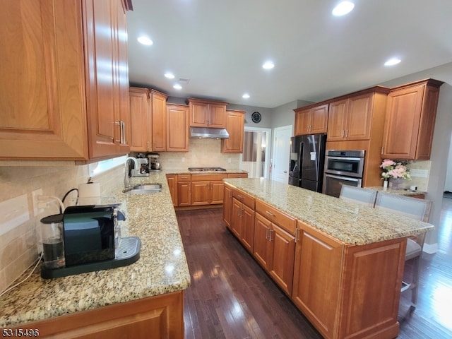 kitchen featuring dark hardwood / wood-style floors, stainless steel appliances, a breakfast bar, light stone countertops, and a center island