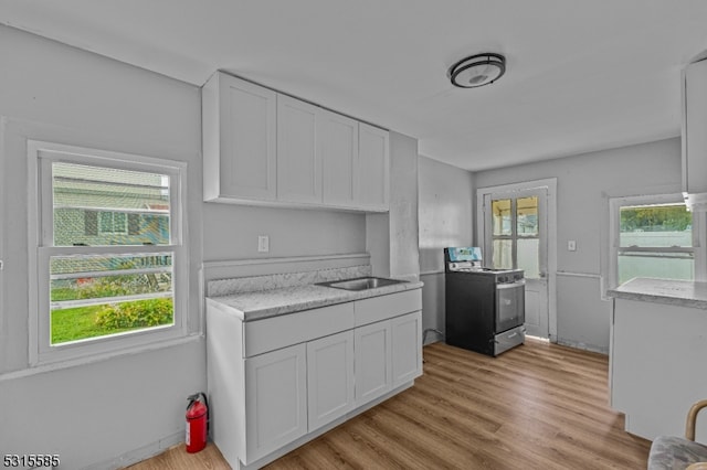 kitchen featuring stainless steel stove, light wood-type flooring, white cabinetry, and a healthy amount of sunlight