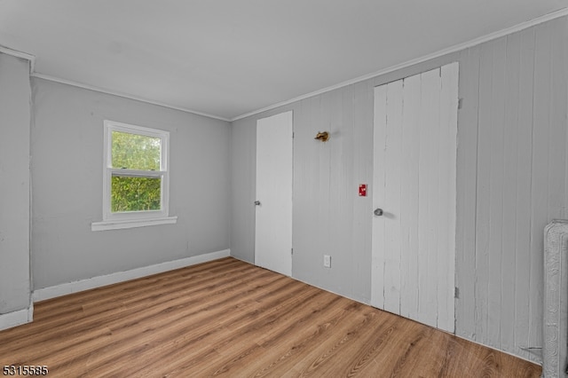 unfurnished room featuring hardwood / wood-style flooring, wooden walls, crown molding, and radiator heating unit