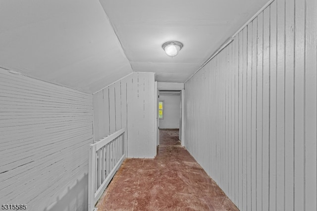 hallway featuring carpet floors, wood walls, and vaulted ceiling