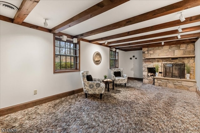 carpeted living room with beamed ceiling and a stone fireplace