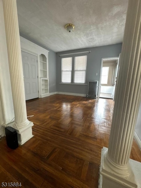 empty room featuring dark parquet flooring, a textured ceiling, and ornate columns