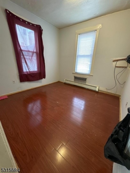 unfurnished room with baseboard heating and hardwood / wood-style floors