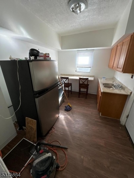 kitchen featuring a textured ceiling, sink, dark wood-type flooring, and stainless steel refrigerator