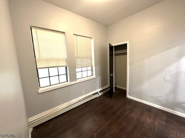 unfurnished bedroom featuring a closet, baseboard heating, and dark hardwood / wood-style floors