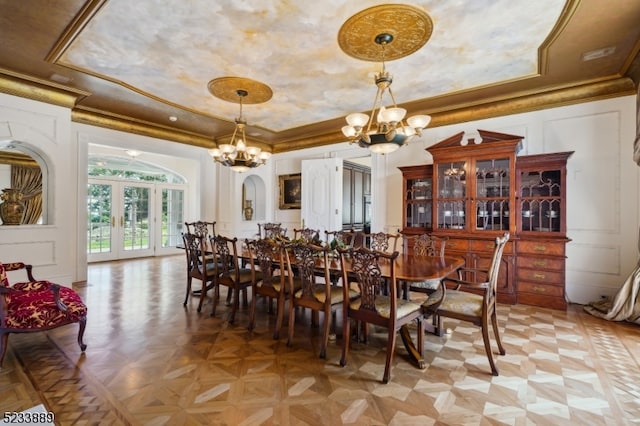 dining space featuring a notable chandelier, a tray ceiling, light parquet flooring, and crown molding