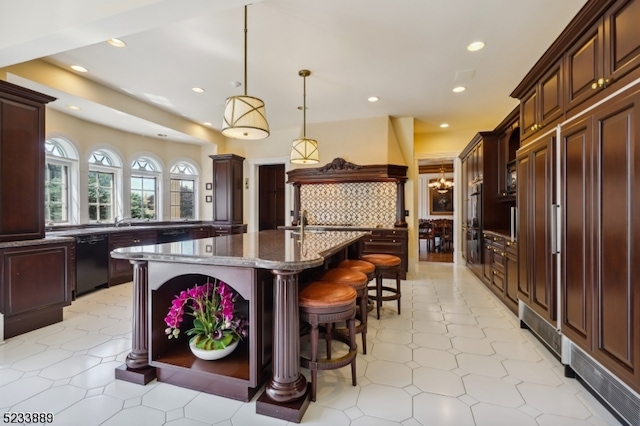 kitchen with dark stone countertops, a breakfast bar, dishwasher, pendant lighting, and a center island with sink