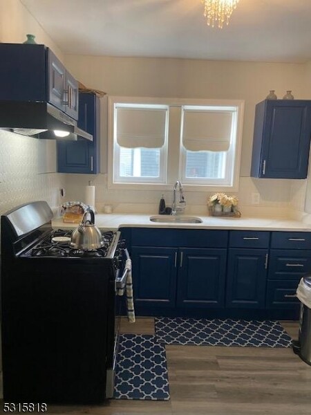 kitchen featuring blue cabinets, black range with electric cooktop, hardwood / wood-style flooring, sink, and a chandelier