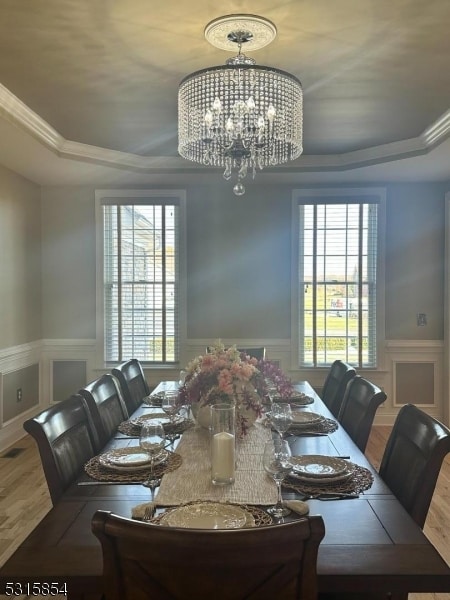 dining space with a raised ceiling, hardwood / wood-style floors, ornamental molding, and a notable chandelier