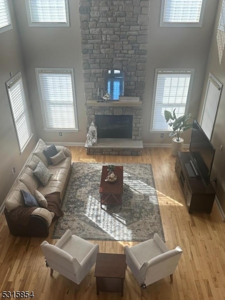 living room featuring a towering ceiling, light hardwood / wood-style flooring, a stone fireplace, and a healthy amount of sunlight