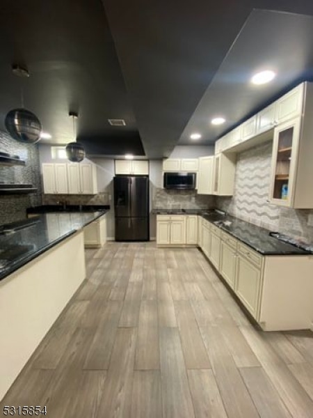 kitchen with tasteful backsplash, sink, black refrigerator, and light wood-type flooring