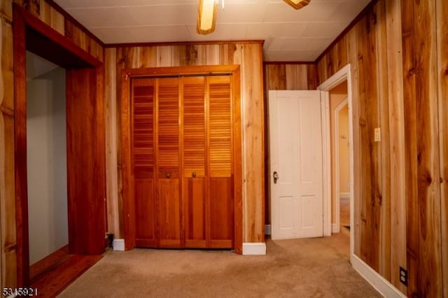 unfurnished bedroom featuring wood walls, a closet, light colored carpet, and ceiling fan