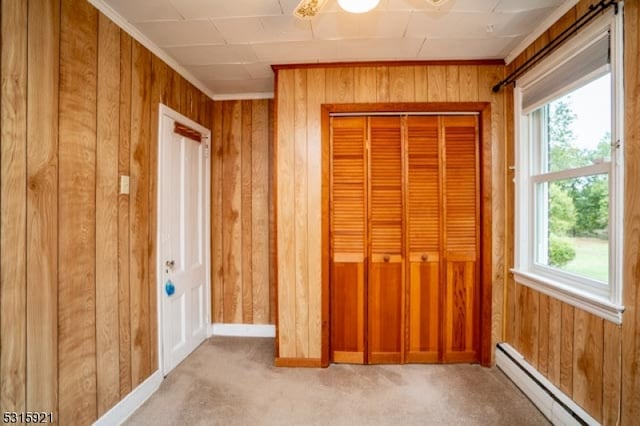 unfurnished bedroom with light colored carpet, baseboard heating, wood walls, and a closet