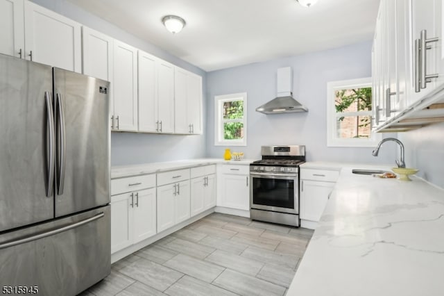 kitchen with light stone counters, white cabinets, stainless steel appliances, sink, and wall chimney range hood