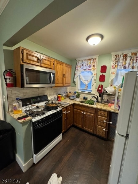 kitchen with light stone counters, dark hardwood / wood-style floors, sink, backsplash, and white appliances