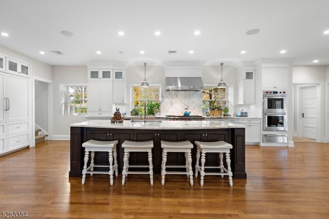 kitchen with double oven, a large island, hanging light fixtures, and dark hardwood / wood-style floors