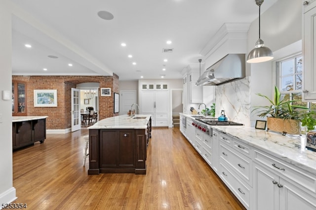 kitchen featuring light hardwood / wood-style floors, stainless steel gas cooktop, pendant lighting, sink, and wall chimney range hood