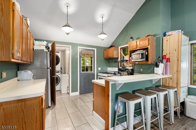 kitchen featuring a kitchen breakfast bar, hanging light fixtures, vaulted ceiling, stainless steel appliances, and stacked washer / dryer