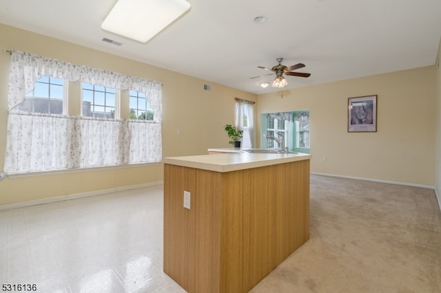 kitchen with ceiling fan, light colored carpet, an island with sink, and sink