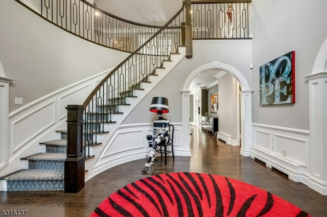 foyer featuring ornate columns, ornamental molding, dark hardwood / wood-style flooring, and a high ceiling