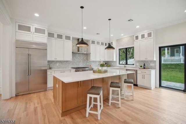 kitchen with appliances with stainless steel finishes, white cabinetry, hanging light fixtures, a center island, and wall chimney exhaust hood