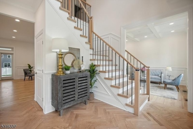 stairs with parquet floors, a towering ceiling, coffered ceiling, and beamed ceiling