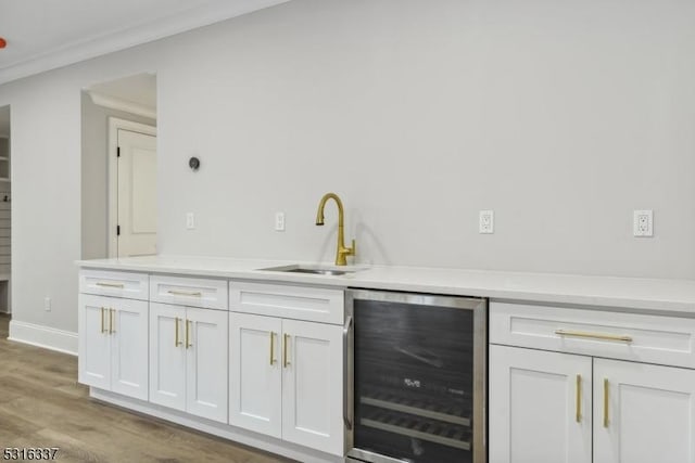 bar featuring white cabinetry, sink, wine cooler, ornamental molding, and light wood-type flooring