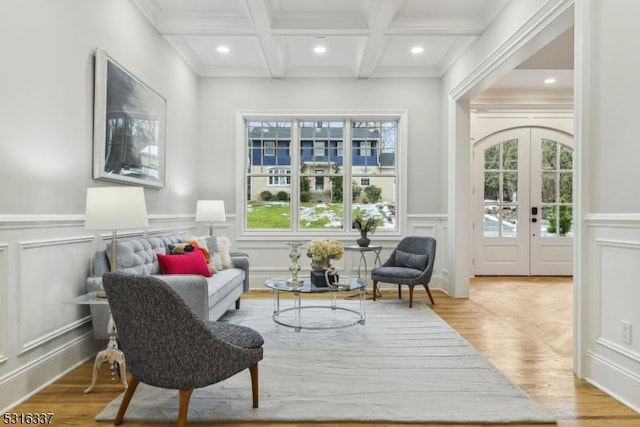 living area with beamed ceiling, coffered ceiling, light hardwood / wood-style floors, and french doors