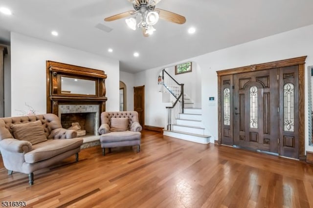 entryway with a fireplace with raised hearth, stairway, ceiling fan, light wood-style flooring, and arched walkways
