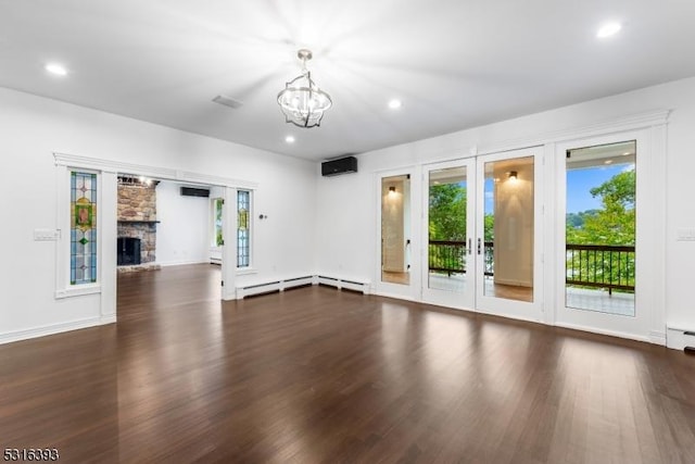 unfurnished living room with a notable chandelier, a wall mounted air conditioner, french doors, a stone fireplace, and wood finished floors