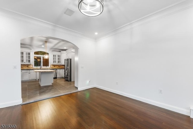 unfurnished living room featuring arched walkways, ornamental molding, and baseboards