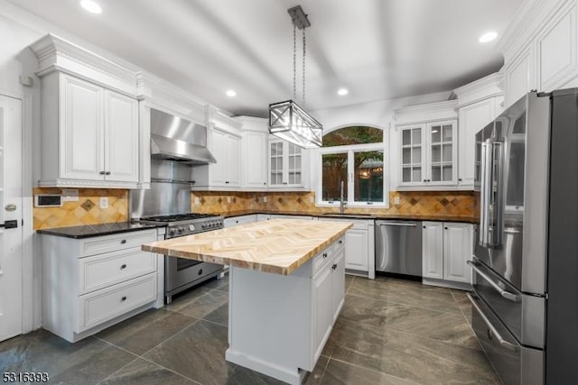 kitchen with a sink, wood counters, high quality appliances, wall chimney exhaust hood, and white cabinets