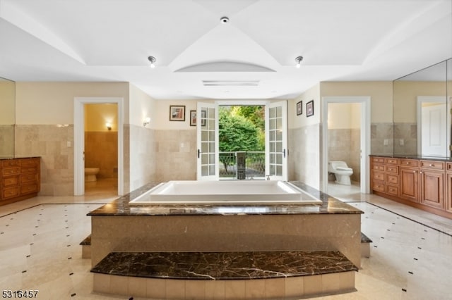 bathroom with a tub to relax in, tile walls, and toilet