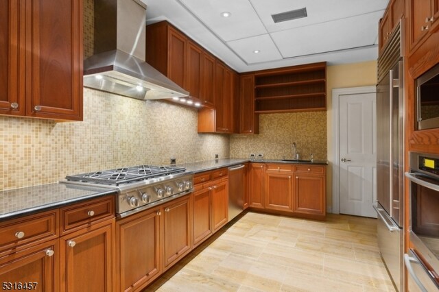 kitchen featuring dark stone counters, sink, wall chimney exhaust hood, stainless steel appliances, and backsplash