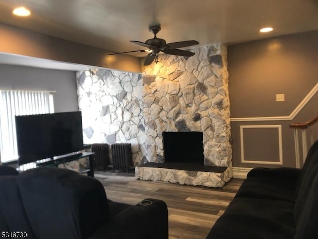 living room with a stone fireplace, ceiling fan, and hardwood / wood-style flooring