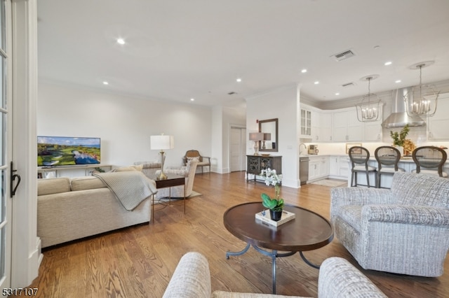 living room featuring light hardwood / wood-style flooring, a chandelier, and ornamental molding