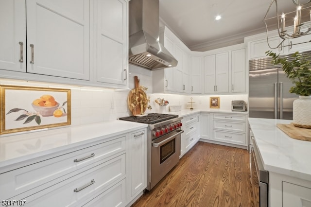 kitchen with white cabinets, premium appliances, wall chimney exhaust hood, dark wood-type flooring, and decorative backsplash