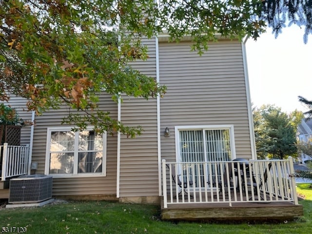 back of house with cooling unit, a wooden deck, and a lawn