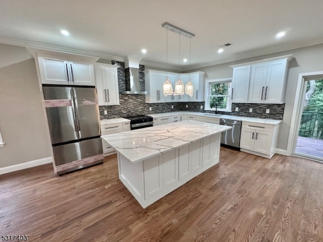 kitchen featuring hanging light fixtures, a kitchen island, wall chimney exhaust hood, stainless steel appliances, and a wealth of natural light