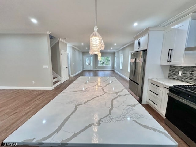 kitchen with appliances with stainless steel finishes, white cabinets, light stone countertops, pendant lighting, and ornamental molding