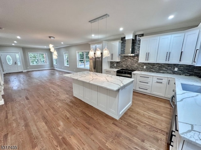 kitchen featuring wall chimney exhaust hood, hanging light fixtures, white cabinetry, and a kitchen island