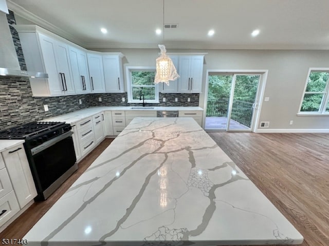 kitchen with pendant lighting, wall chimney range hood, white cabinetry, appliances with stainless steel finishes, and light stone countertops