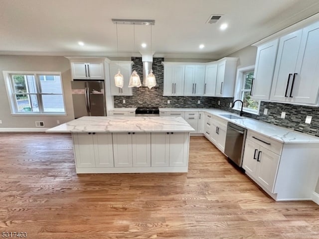 kitchen featuring white cabinets, hanging light fixtures, a kitchen island, wall chimney range hood, and appliances with stainless steel finishes