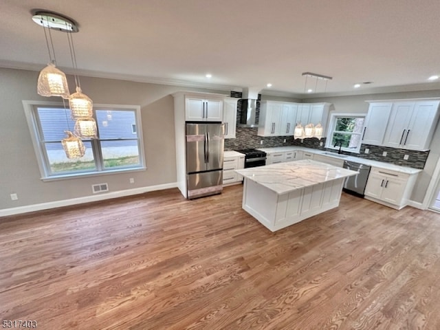 kitchen with hanging light fixtures, white cabinets, stainless steel appliances, a center island, and wall chimney range hood