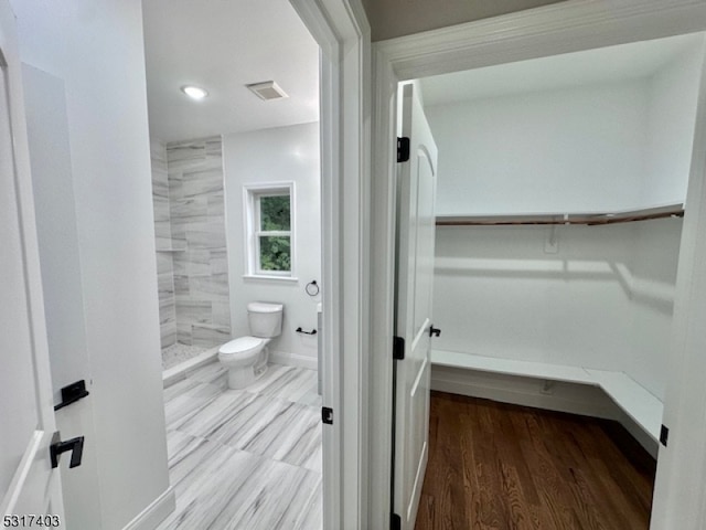 bathroom with hardwood / wood-style flooring, toilet, and tiled shower