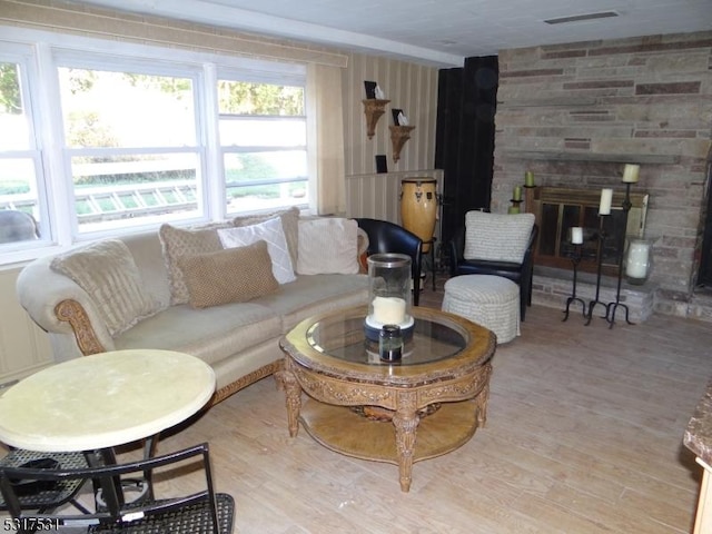 living room with a stone fireplace, wood finished floors, and visible vents